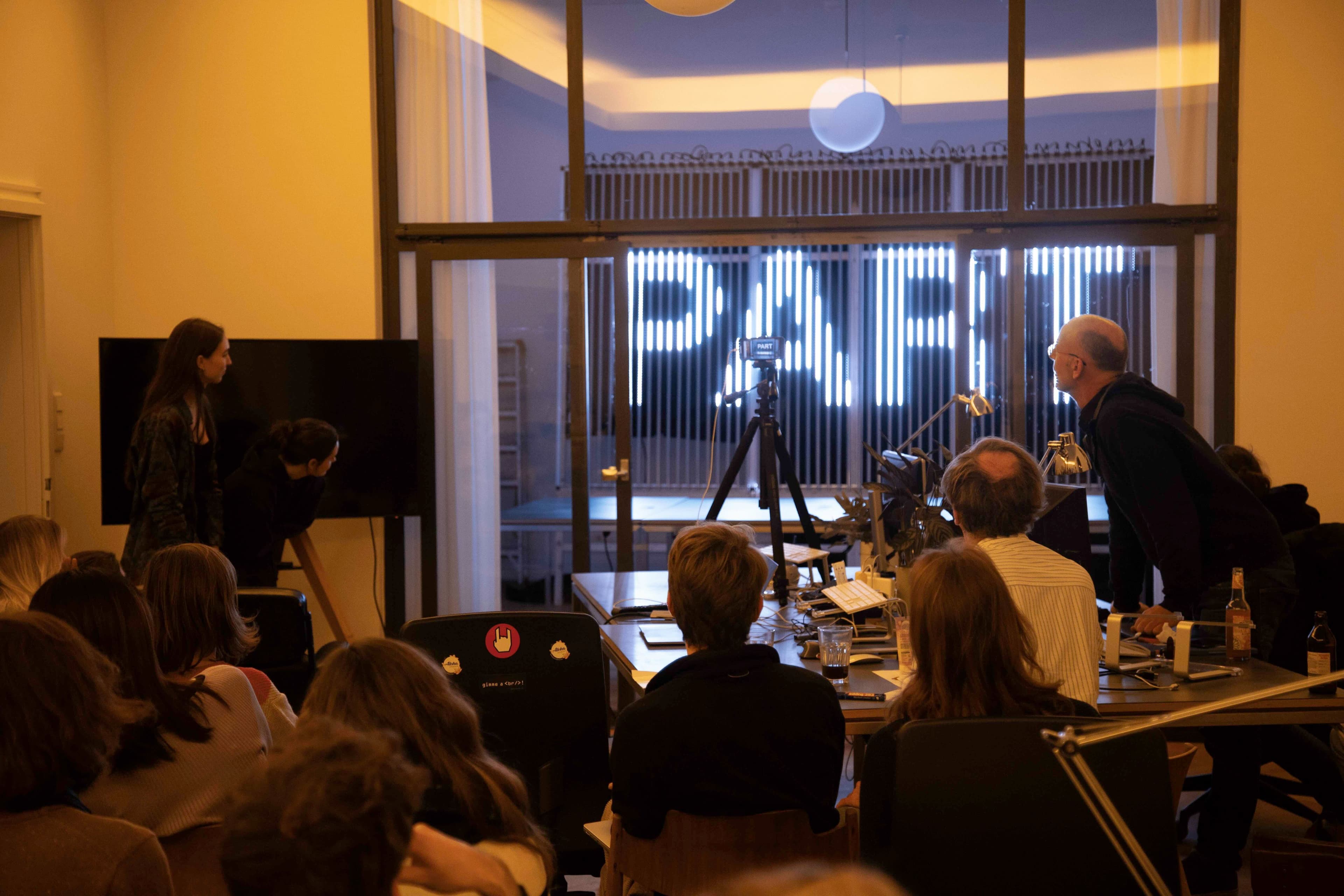 In einem Raum schauen verschiedene Leute auf eine LED-Schrift-Installation.