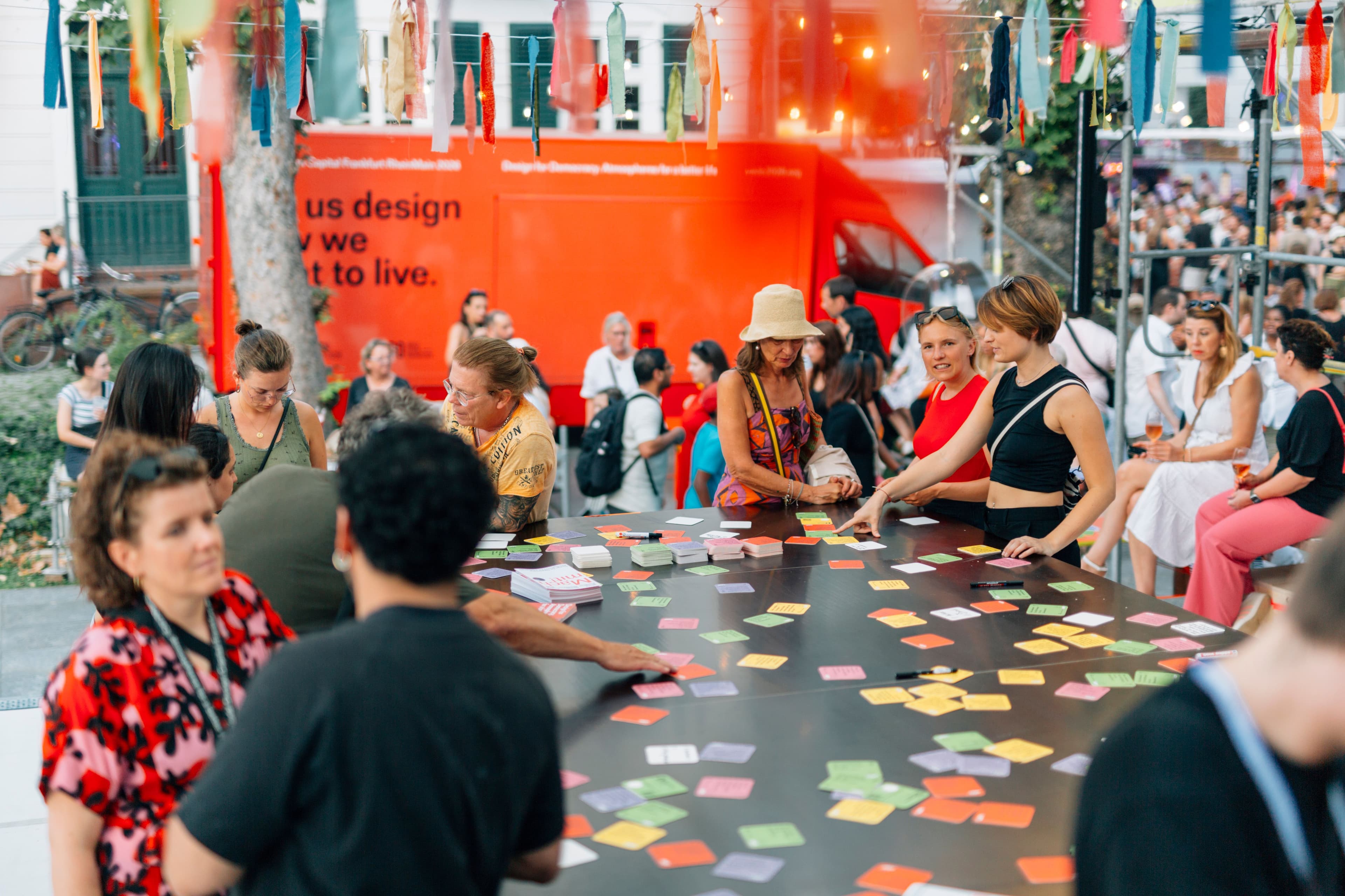 Foto von Menschen, die um einen Tisch mit bunten Demokratiedeckeln stehen