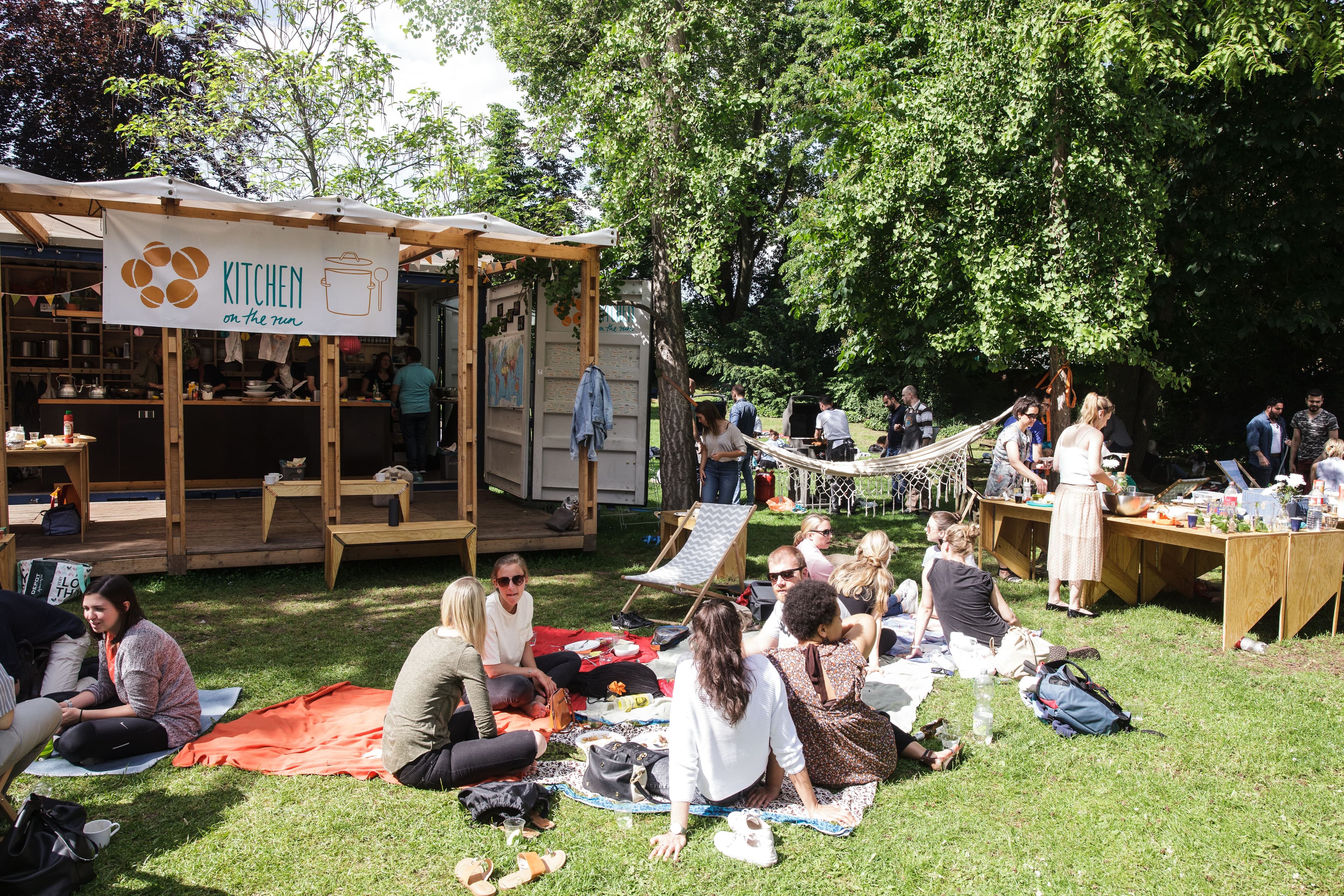 Menschen sitzen auf einer Wiese vor dem Projekt Kitchen on the Run