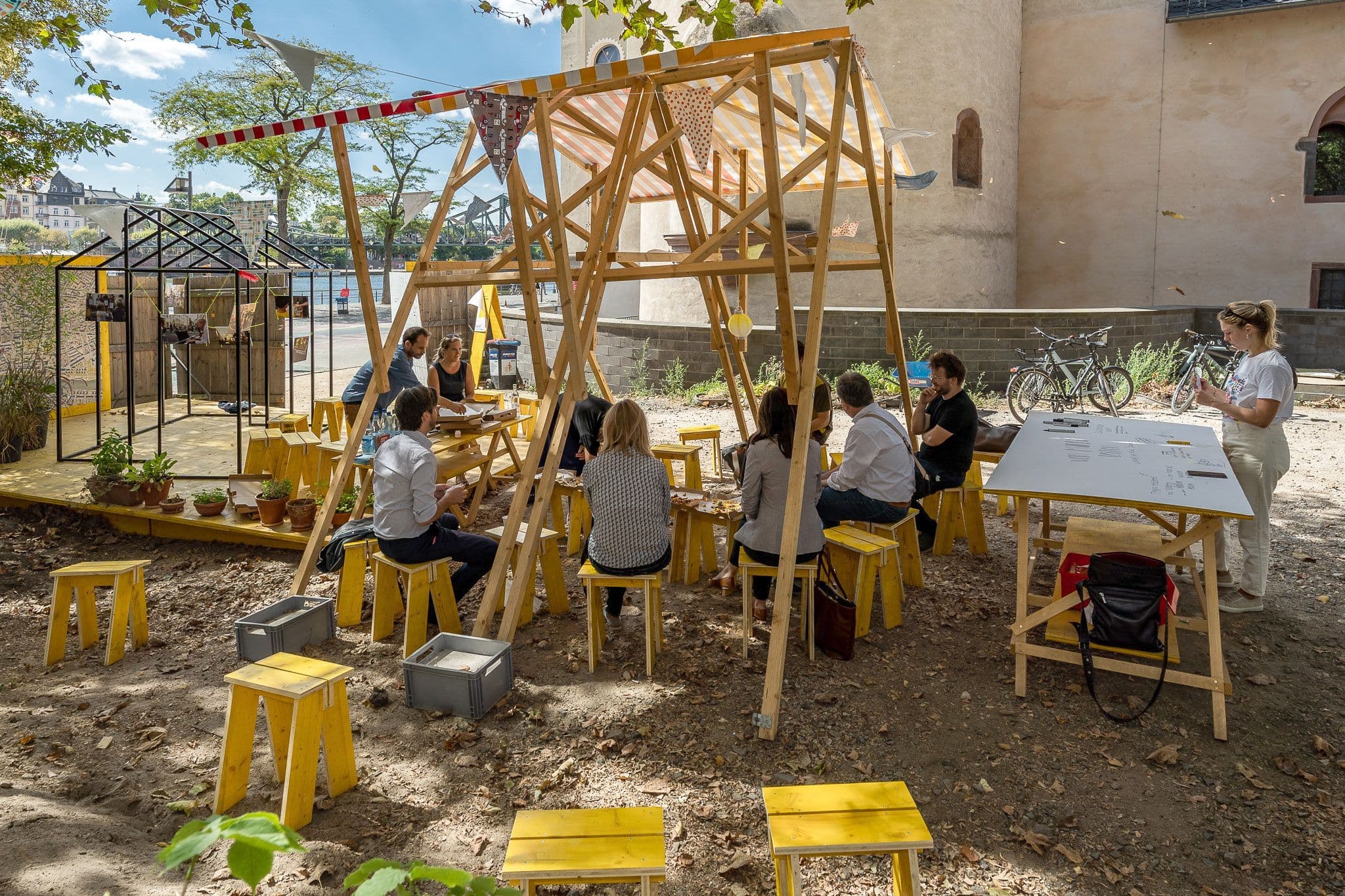 Personen sitzen zusammen unter einer Holzkonstruktion