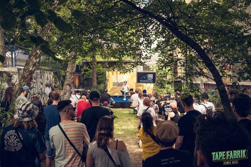 Einige Menschen hören in einem Hinterhof einem Vortrag zu.