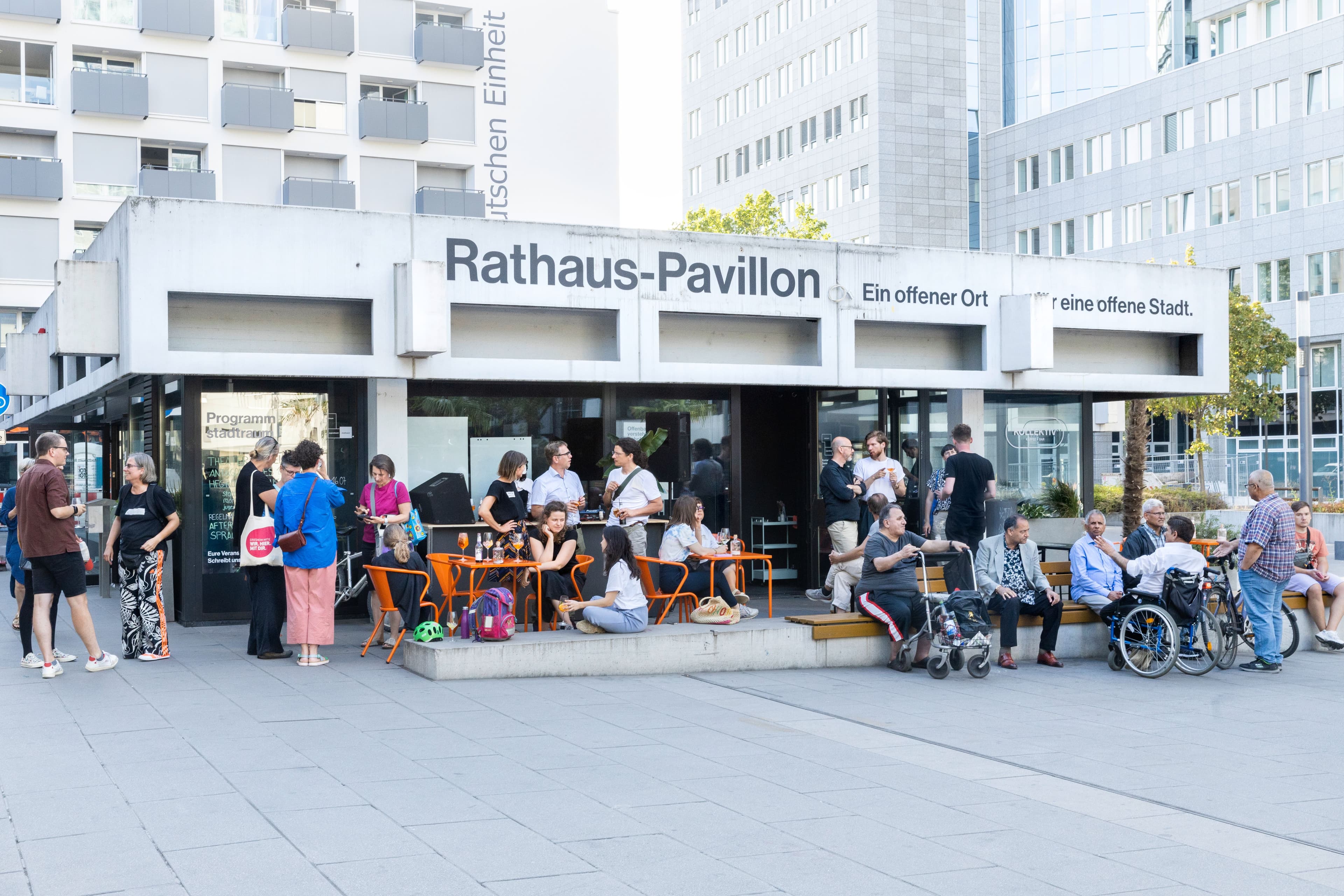 Menschen sitzen vor dem Rathaus-Pavillon in Offenbach