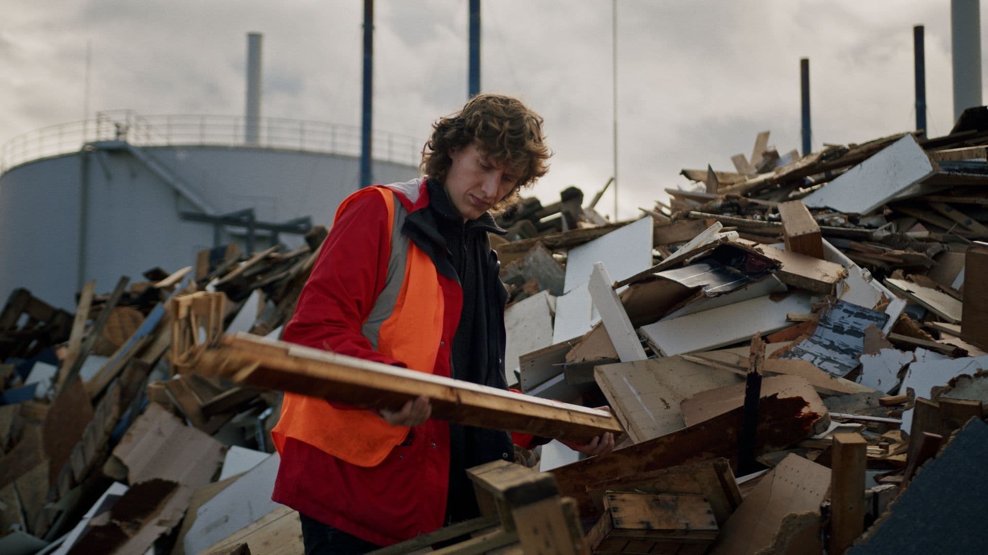 Eine Person mit einem Holzbalken in den Händen vor einem Haufen von Holzabfällen