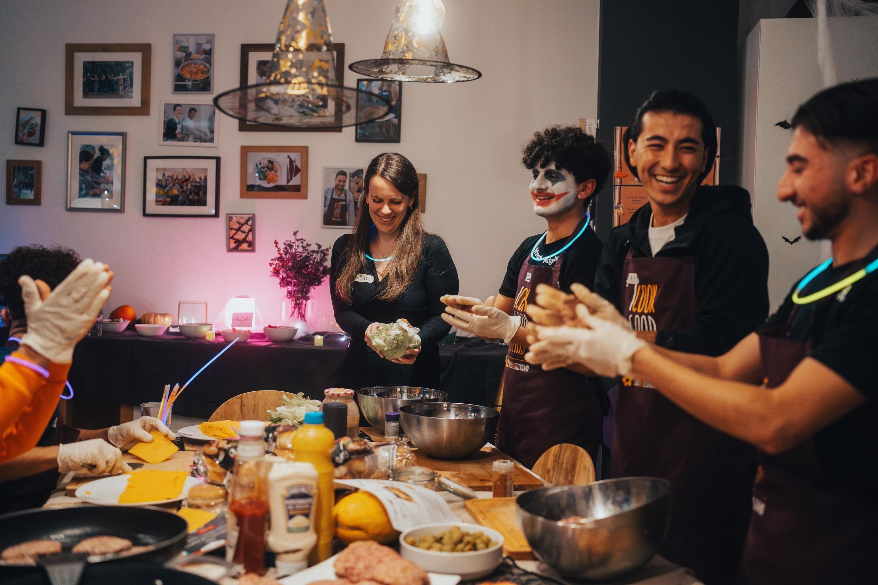 Mehrere Personen stehen um einen Tisch herum und kochen gemeinsam und lachen.
