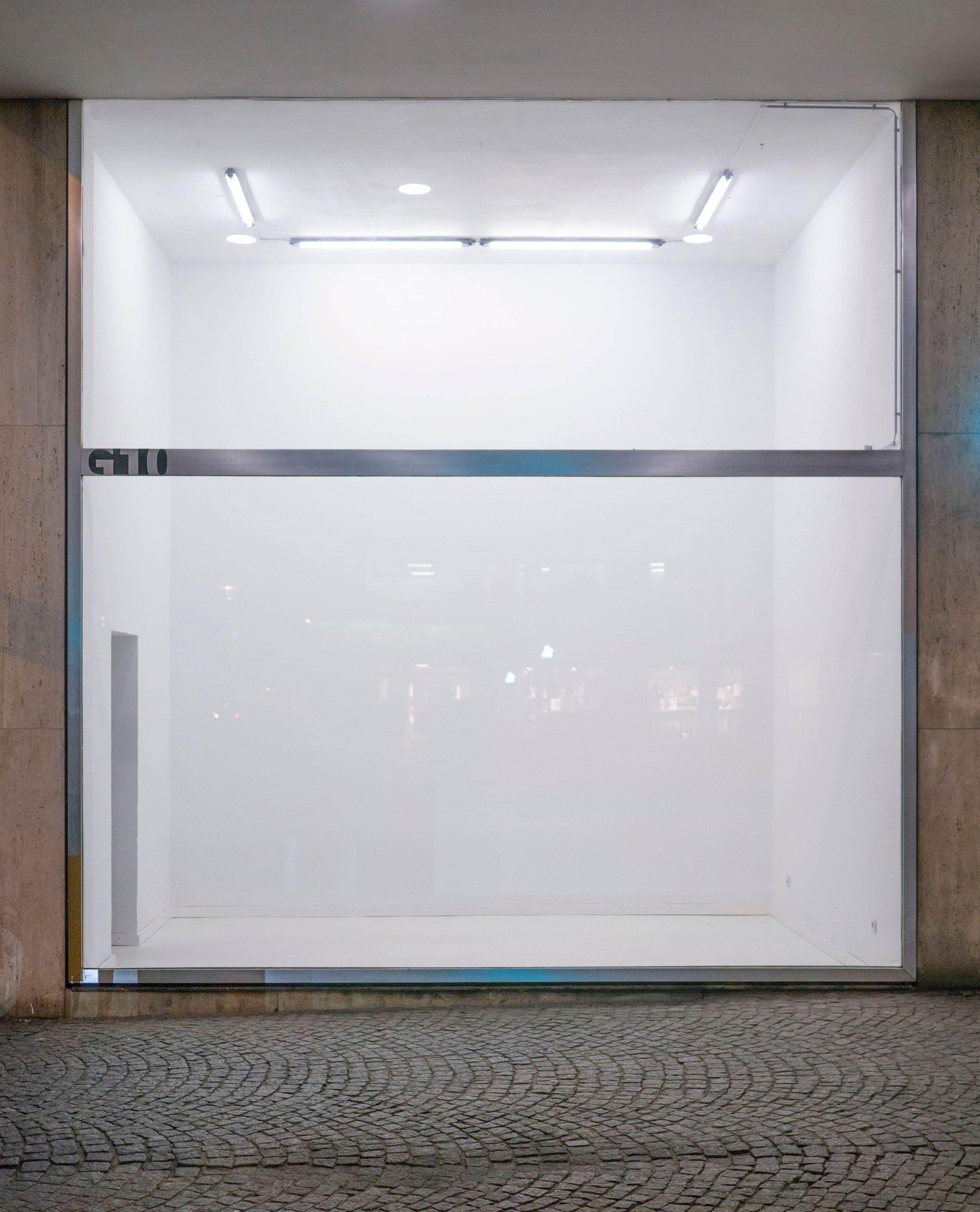 Von außen ist ein leerer, beleuchteter Ausstellungsraum zu sehen.