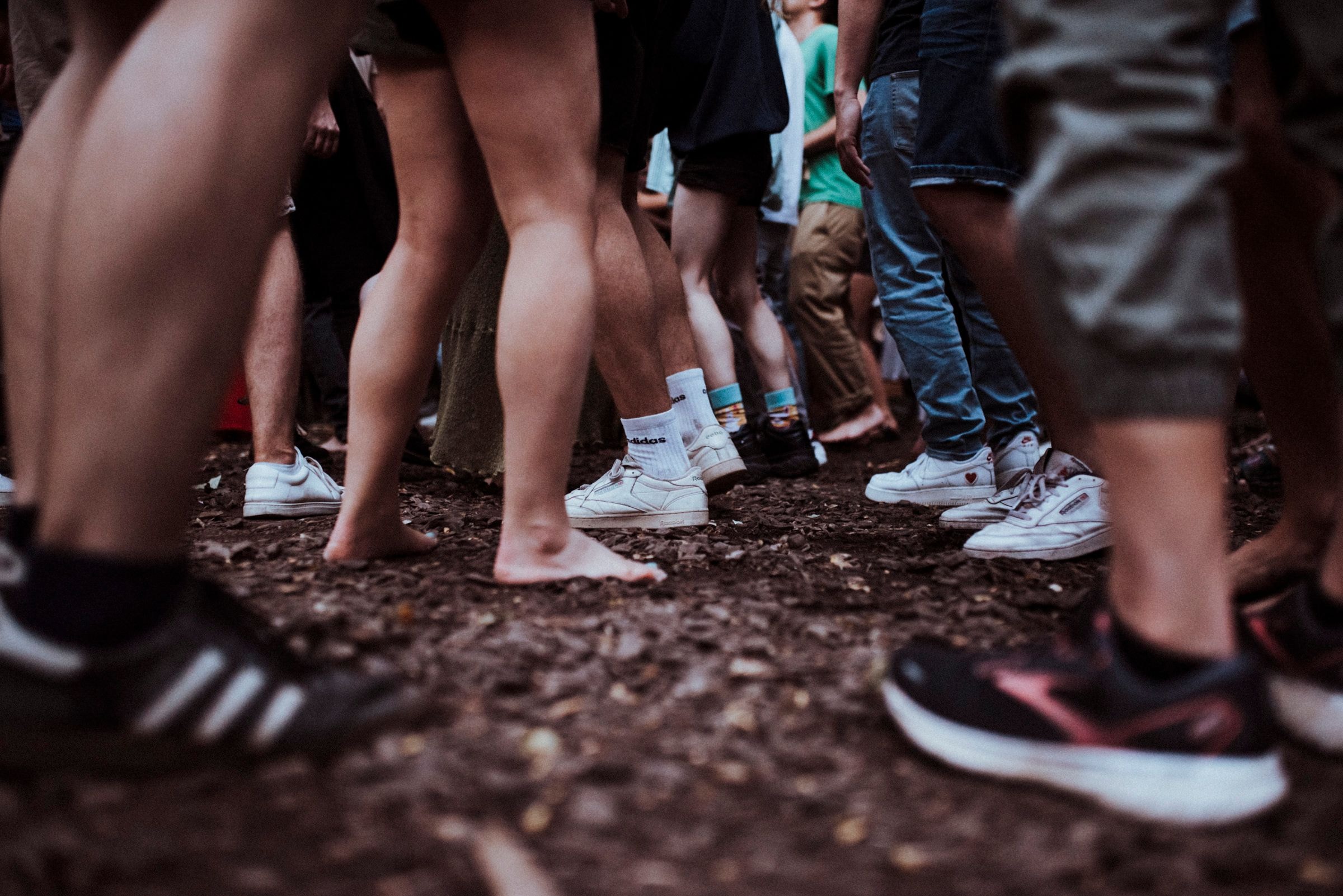 Zu sehen sind die Beine verschiedener Menschen, die auf der Erde stehen.