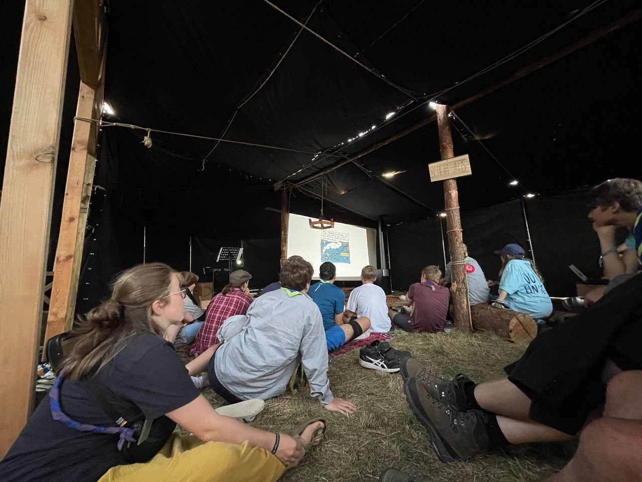 Menschen sitzen vor einer Leinwand am Boden mit Heu