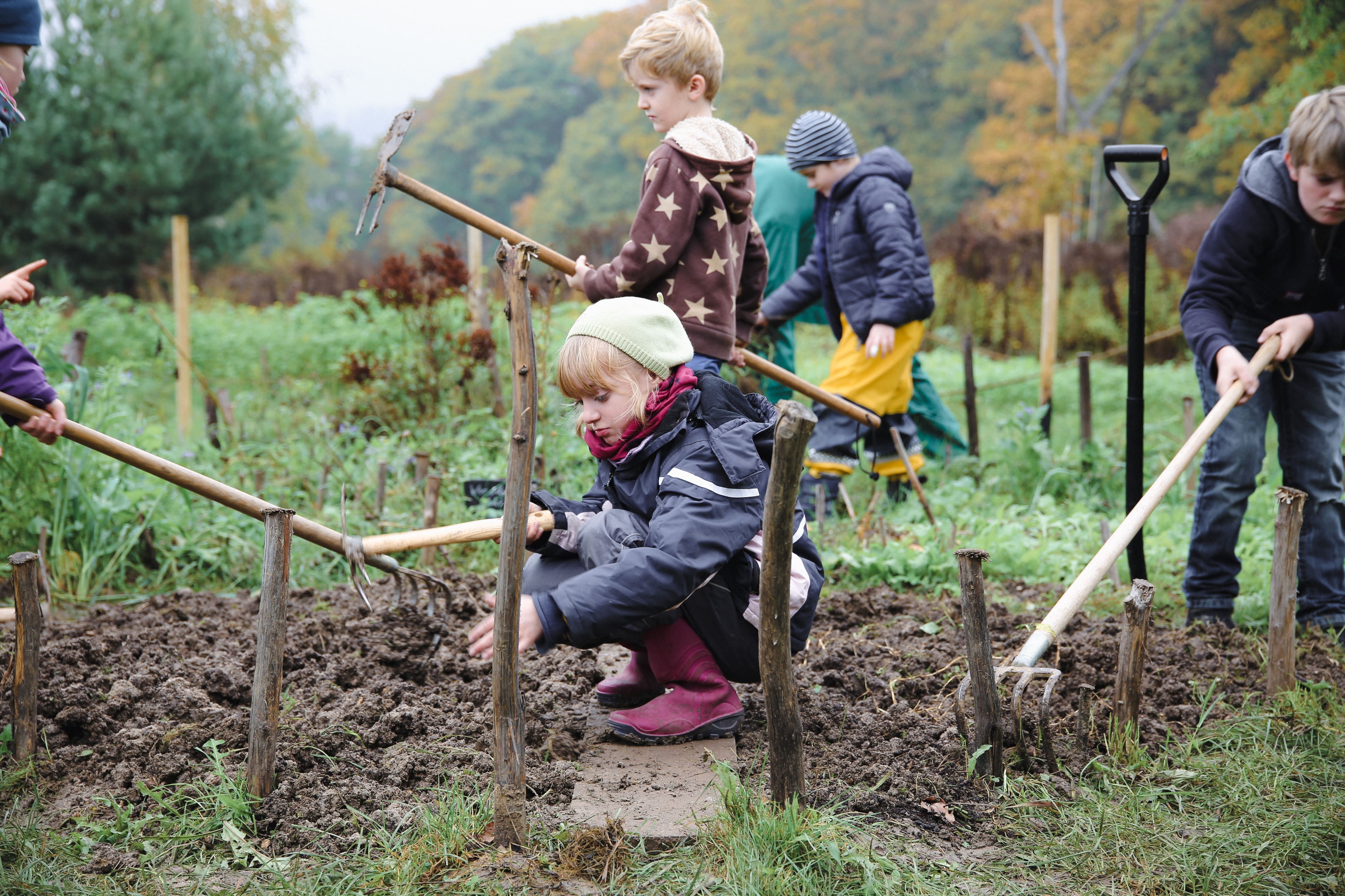 Kinder arbeiten mit Gartenhandwerkzeugen auf einer Wiese.