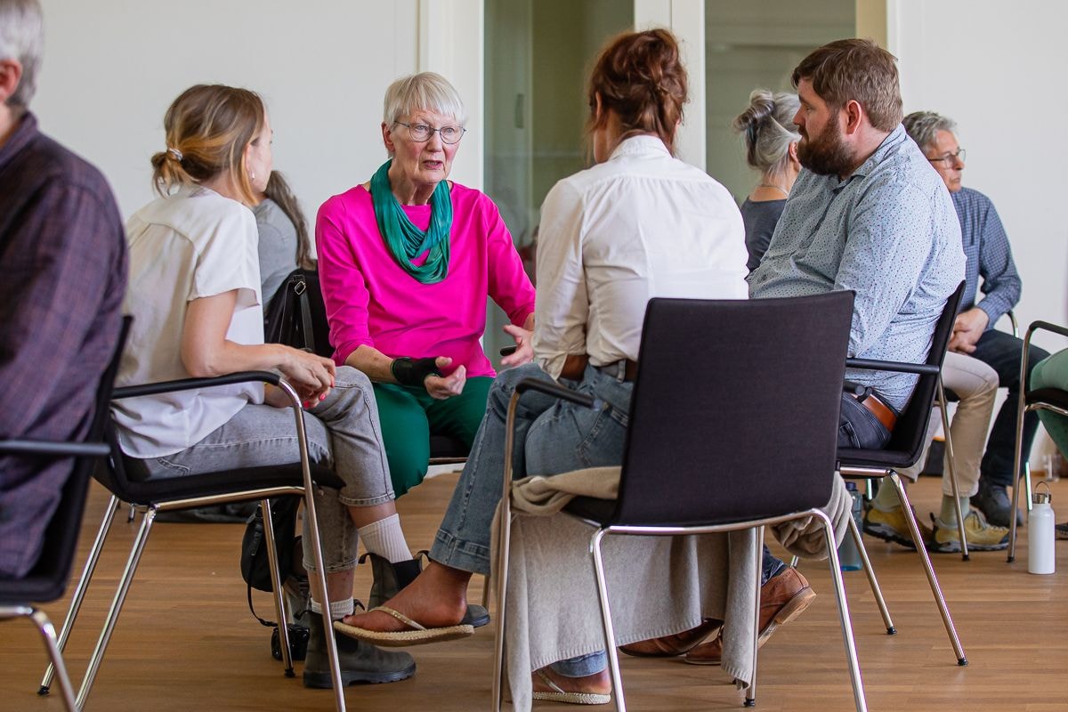vier Menschen sitzen in einem Stuhlkreis und unterhalten sich mit einander
