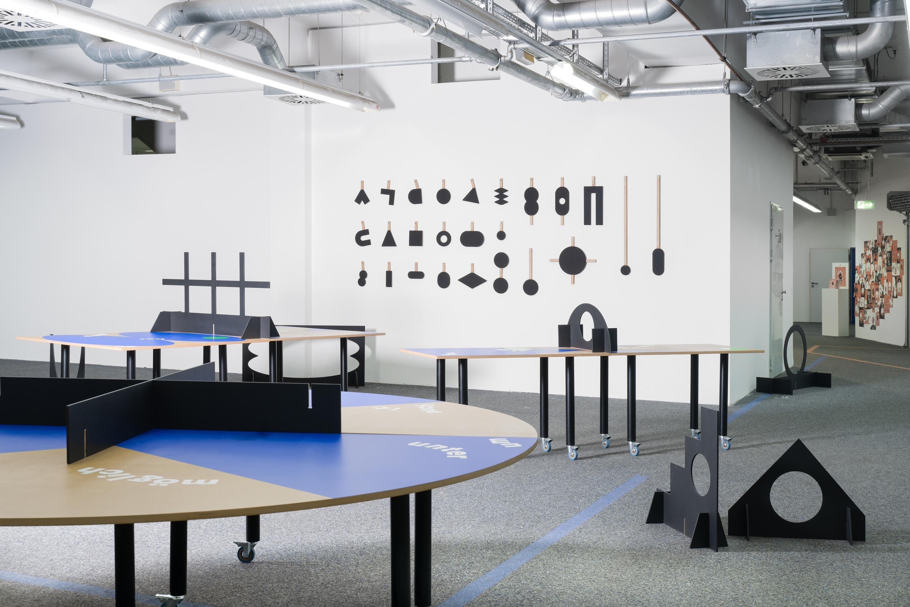 Eine Runde Tischtennisplatte steht vor einer Wand, an der viele unterschiedliche Schläger hängen. 