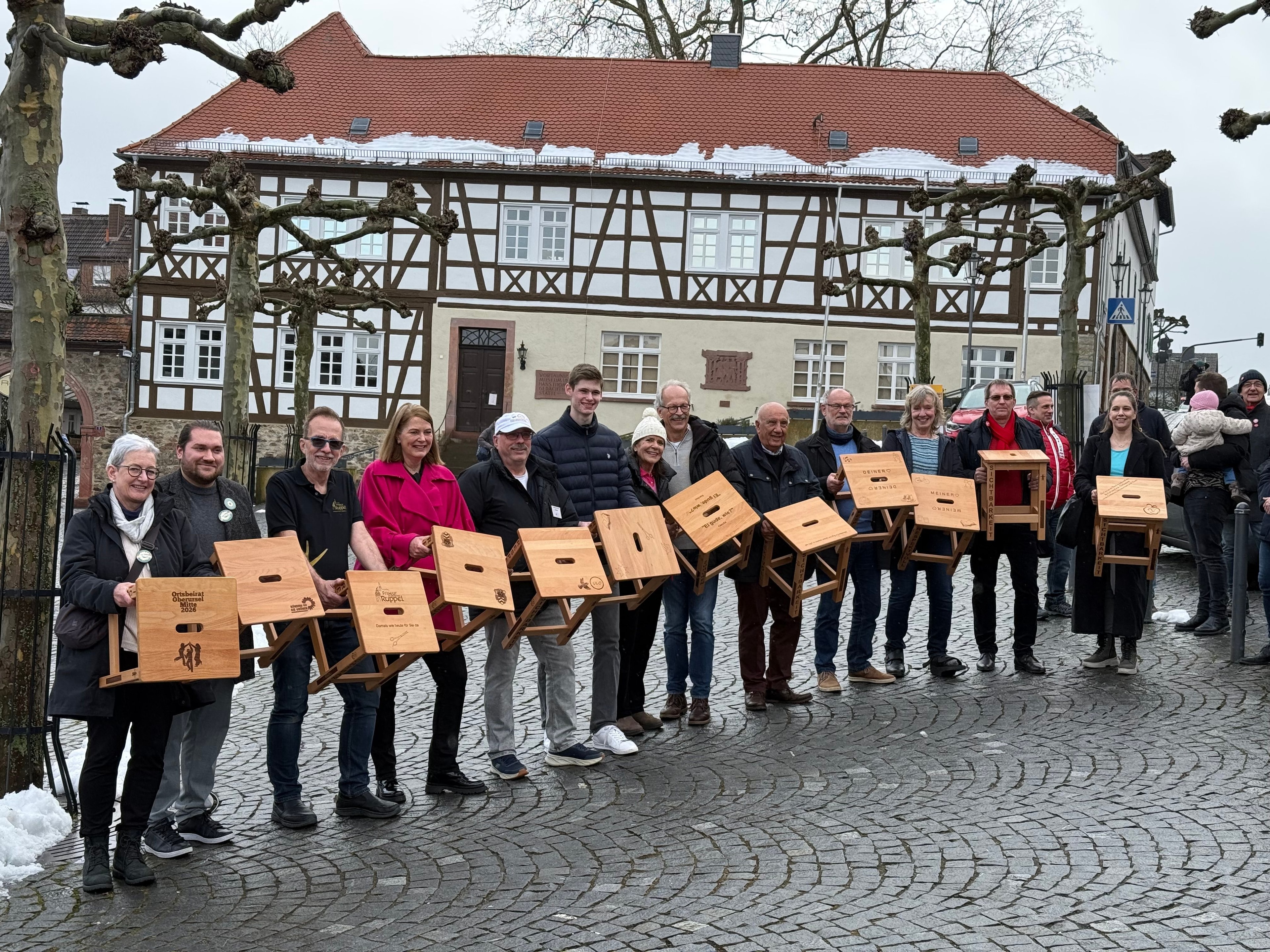 Menschen halten ihre Hocker auf dem Marktplatz Oberursel in die Kamera