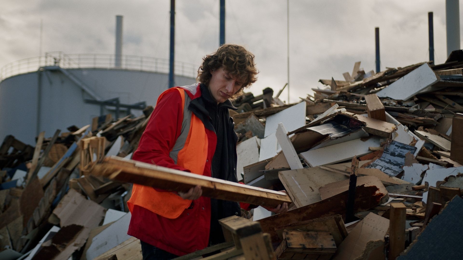 Eine Person mit einem Holzbalken in den Händen vor einem Haufen von Holzabfällen
