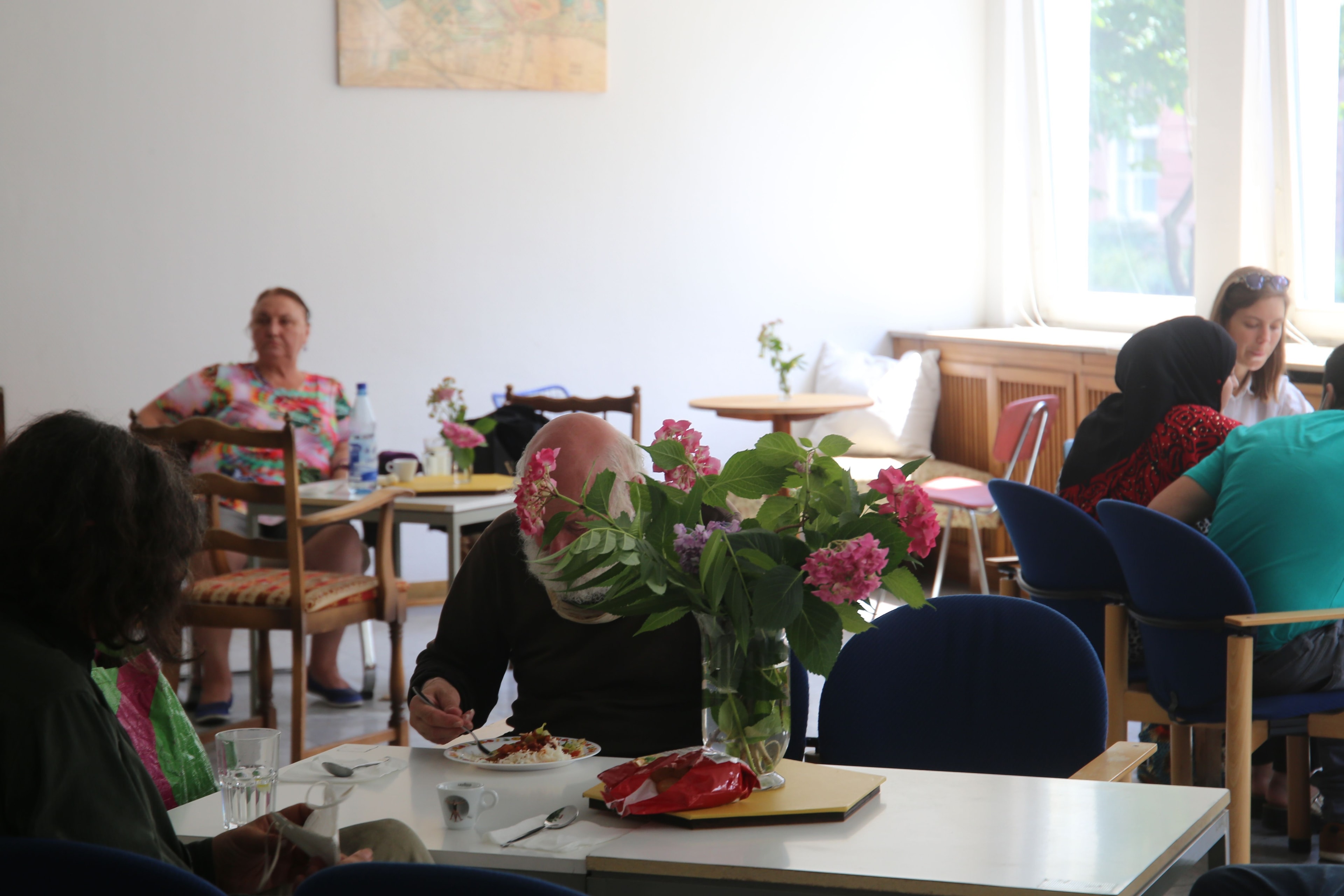 In einem Raum sitzen Menschen an verschiedenen Tischen zusammen und essen.