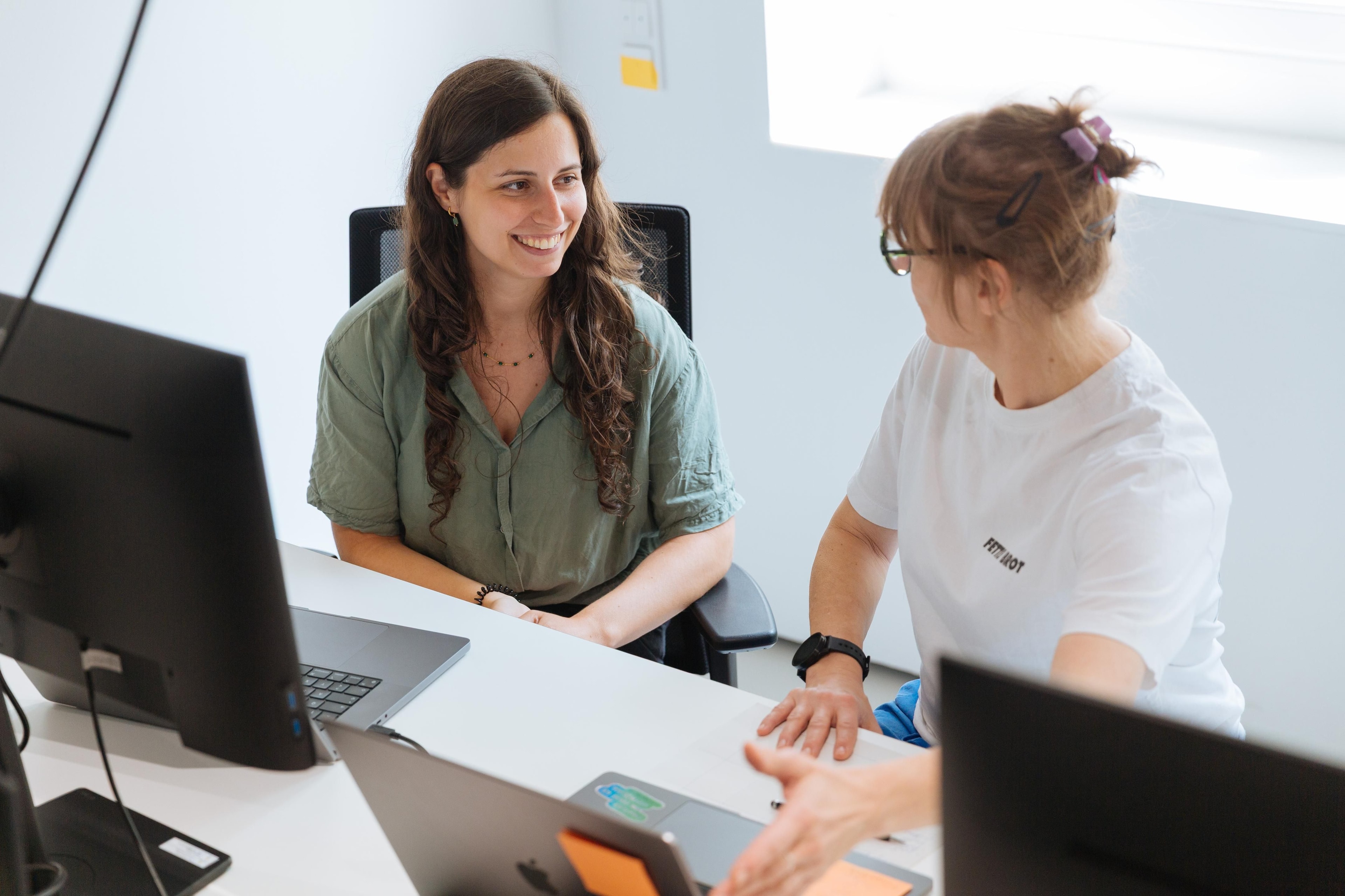Zwei Personen sitzen nebeneinander im Büro und schauen einander an.