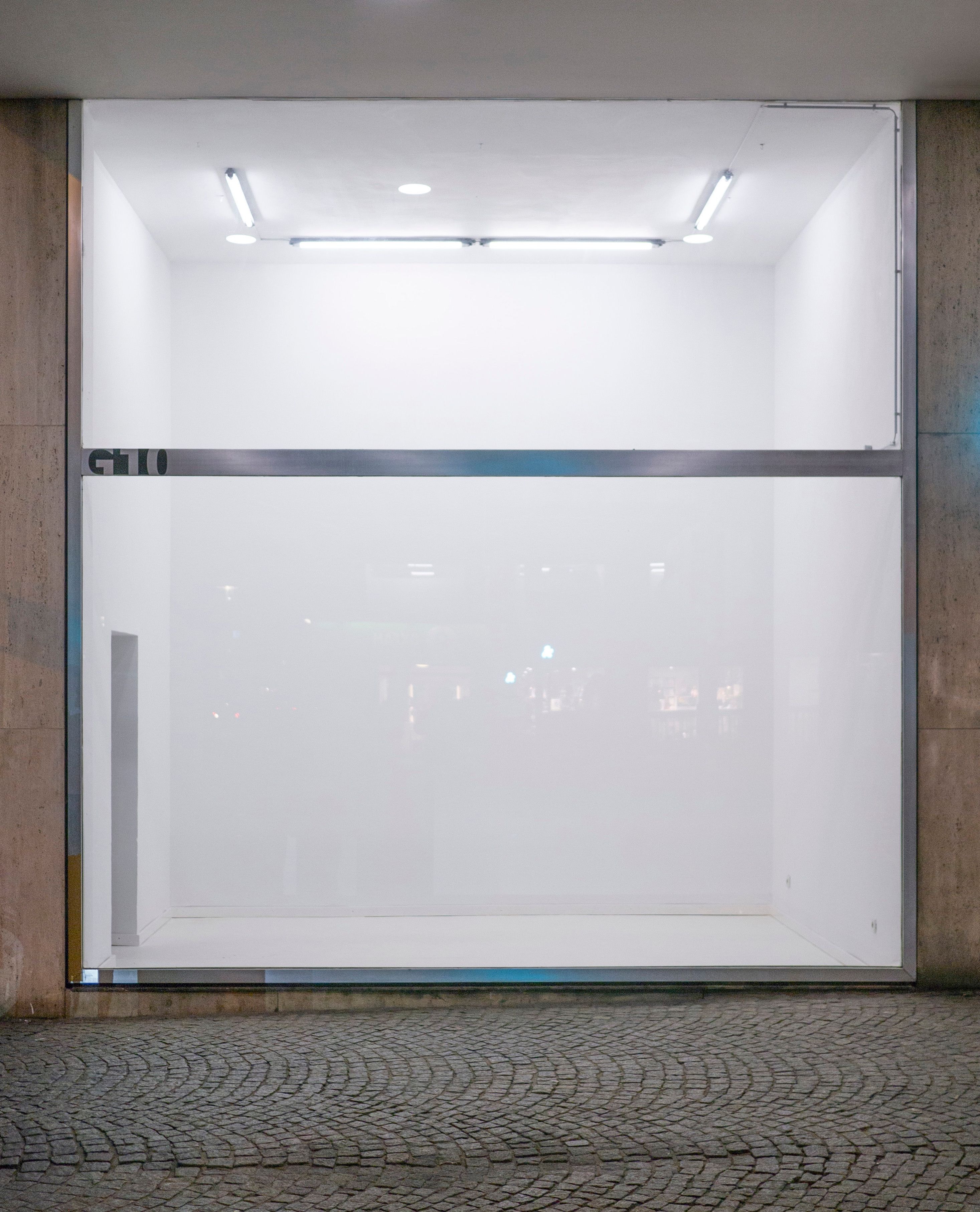 Von außen ist ein leerer, beleuchteter Ausstellungsraum zu sehen.