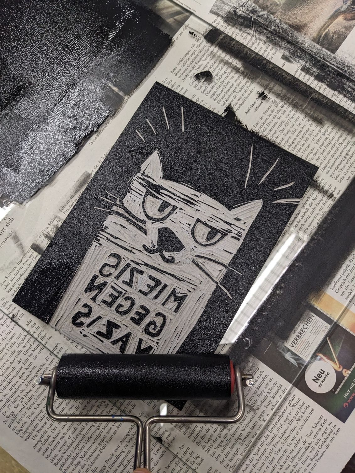 Eine Linoldruckvorlage von einer Katze liegt zusammen mit einer Linolrolle auf einem Tisch.