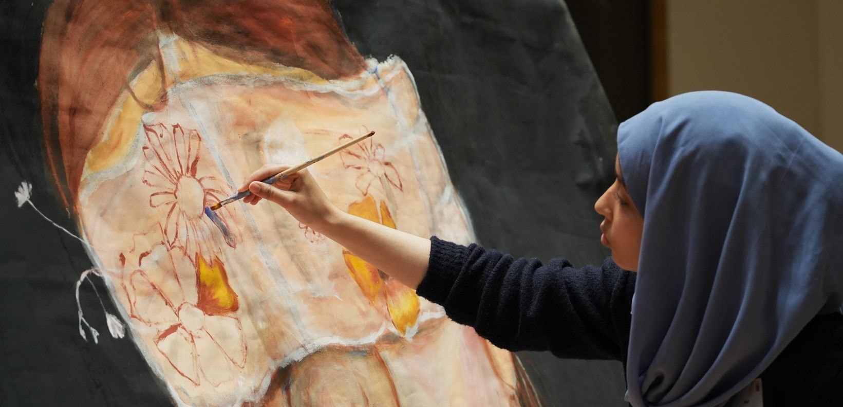 Frau sitzt vor einem Gemälde und malt