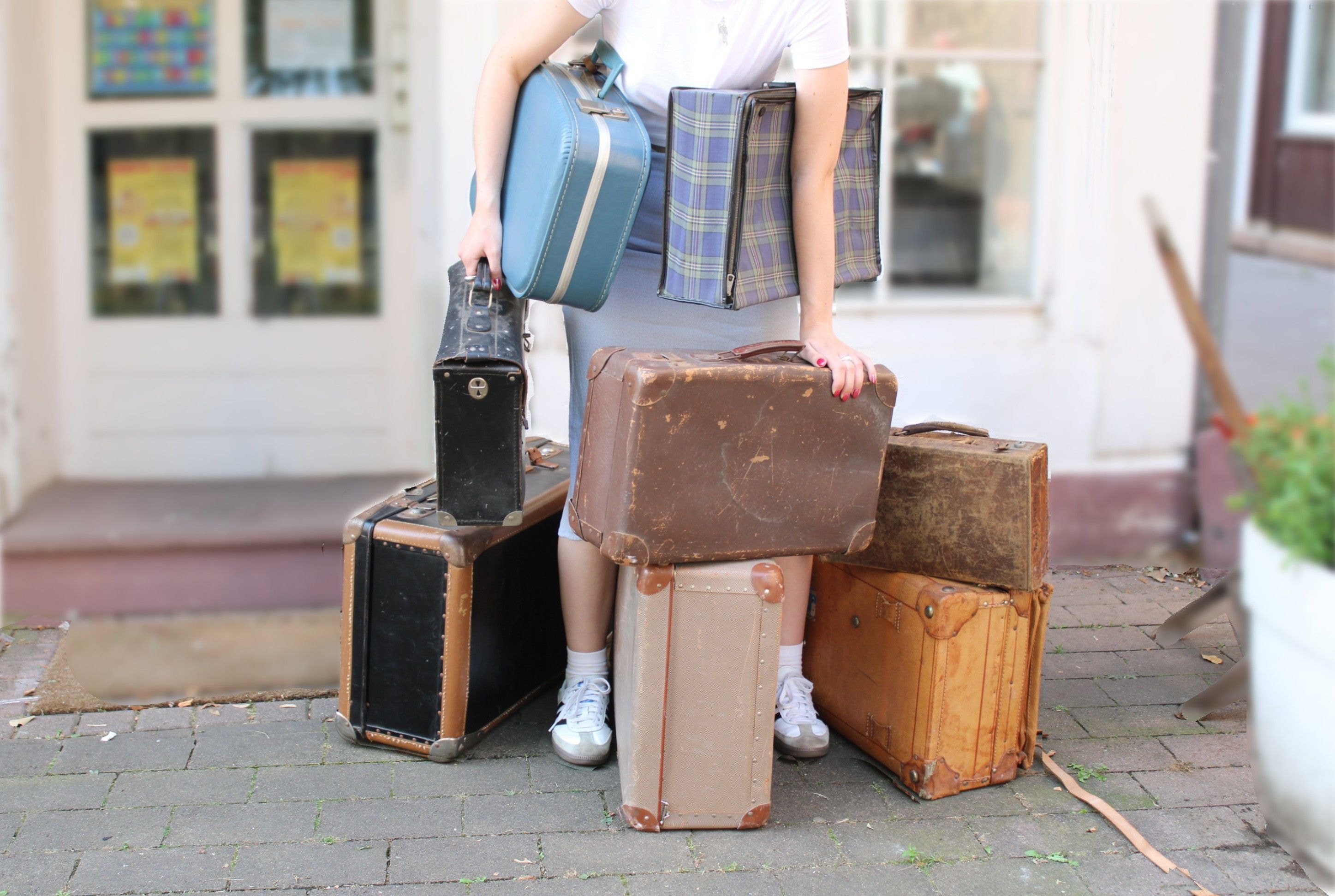 Eine Person steht mit zahlreichen Koffern vor einer Haustür.