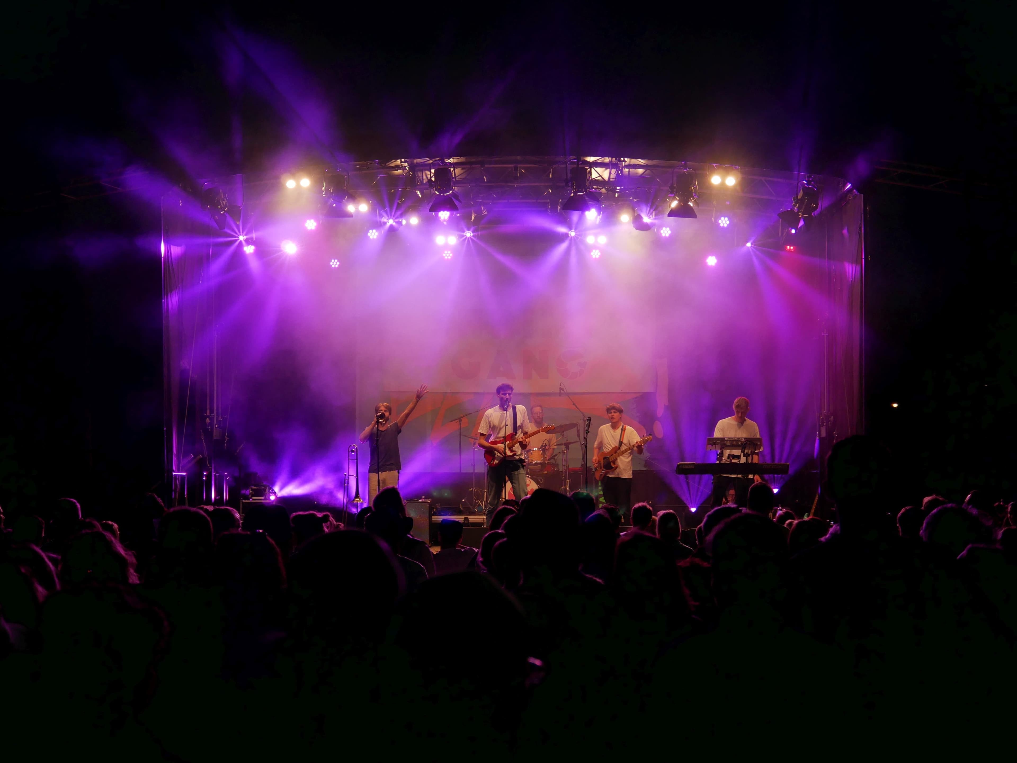 Eine lila beleuchtete Bühne erstrahlt im Licht und beleuchtet sowohl die Band als auch das Publikum.