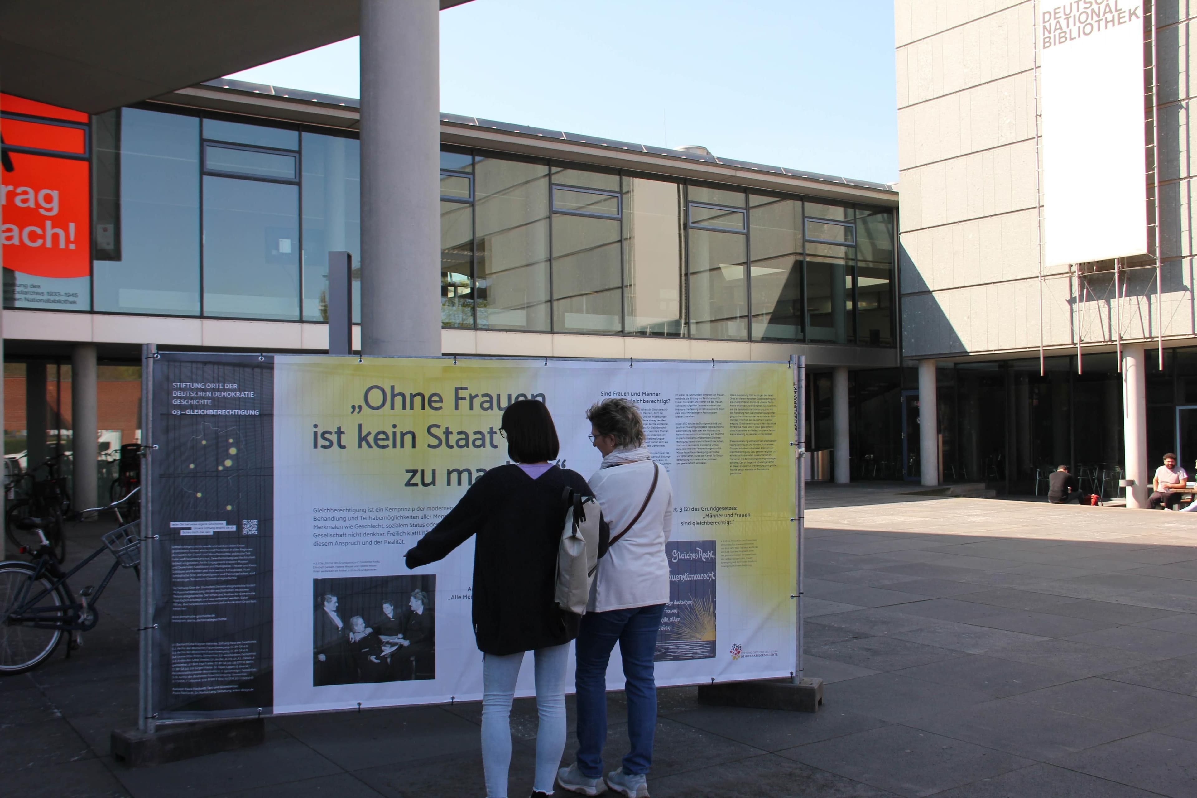 Menschen stehen vor einem Infoplakat auf einem Bauzaun