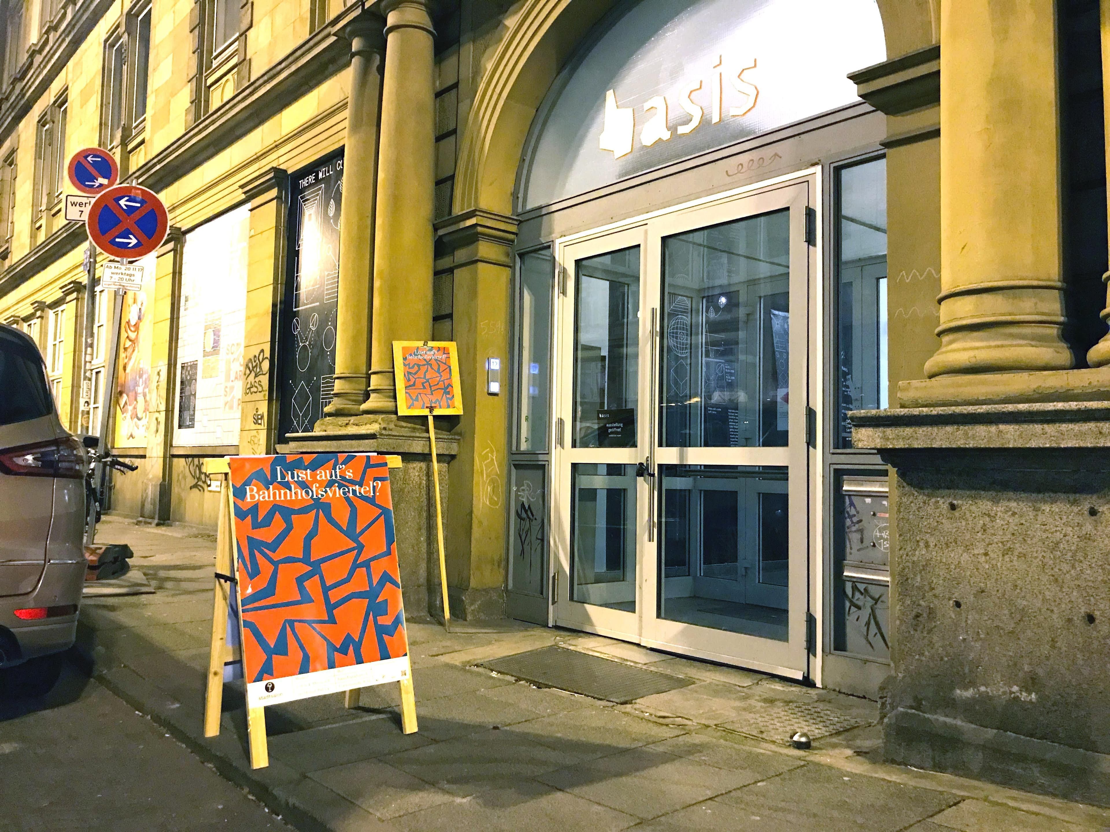 Vor einer großen Glastür steht ein Aufsteller mit einem Poster, auf dem die Frage „Lust auf das Bahnhofsviertel?” steht.